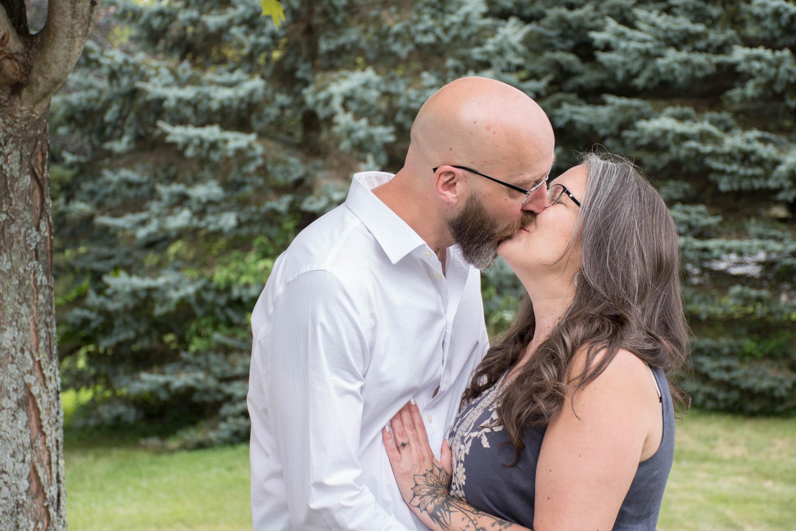 Scott and Wendy kissing in front of a background of trees